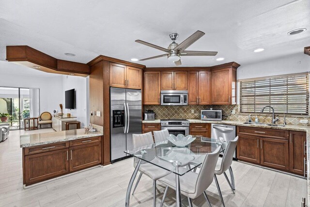 kitchen with appliances with stainless steel finishes, light wood-type flooring, light stone counters, ceiling fan, and sink