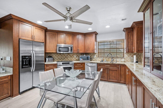 kitchen with sink, light stone countertops, appliances with stainless steel finishes, tasteful backsplash, and light hardwood / wood-style floors