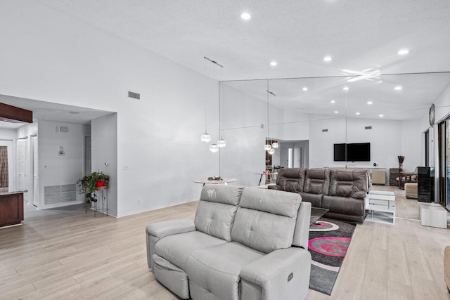 living room featuring a textured ceiling, light wood-type flooring, and high vaulted ceiling