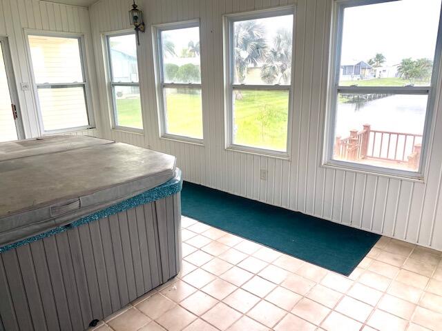 unfurnished sunroom with a water view, a hot tub, and a healthy amount of sunlight