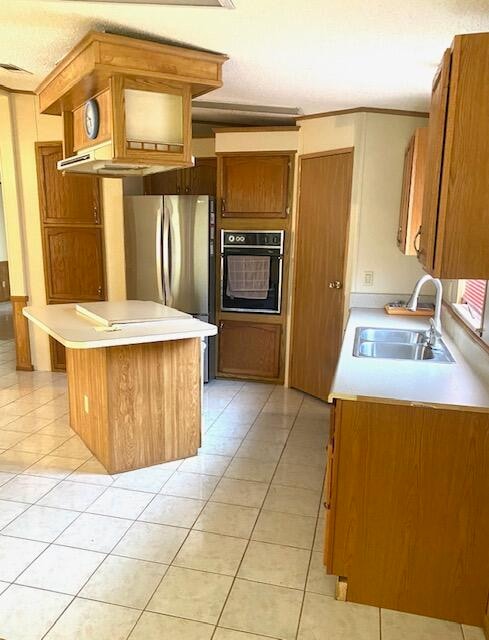 kitchen featuring light tile patterned floors, black oven, stainless steel refrigerator, and sink