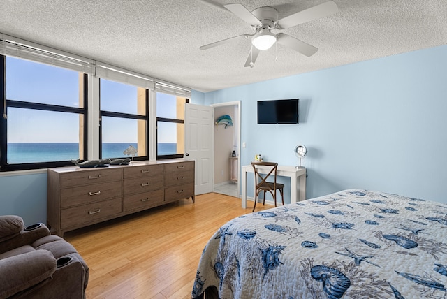 bedroom featuring a textured ceiling, a water view, light hardwood / wood-style flooring, and ceiling fan