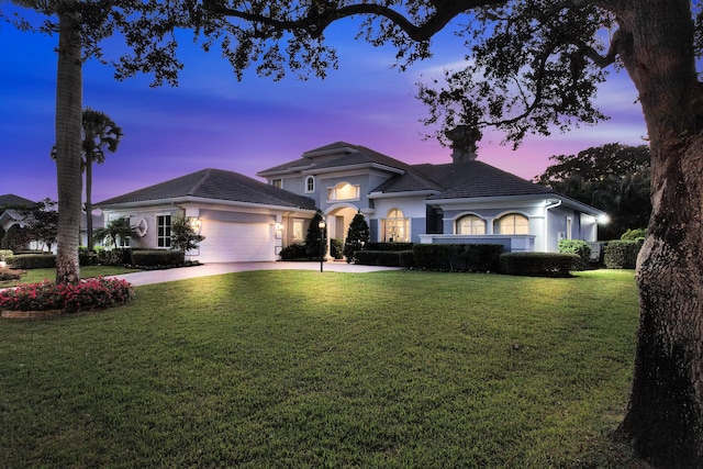 view of front of house with stucco siding, driveway, a front yard, a garage, and a tiled roof