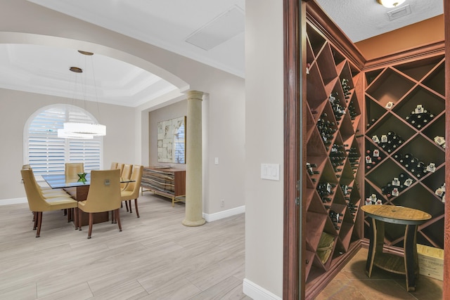 wine cellar with decorative columns, visible vents, arched walkways, light wood-style flooring, and a tray ceiling