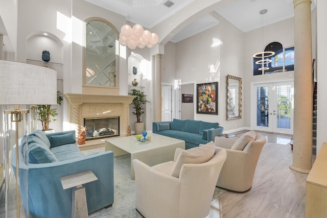 living room with french doors, crown molding, an inviting chandelier, a towering ceiling, and a high end fireplace