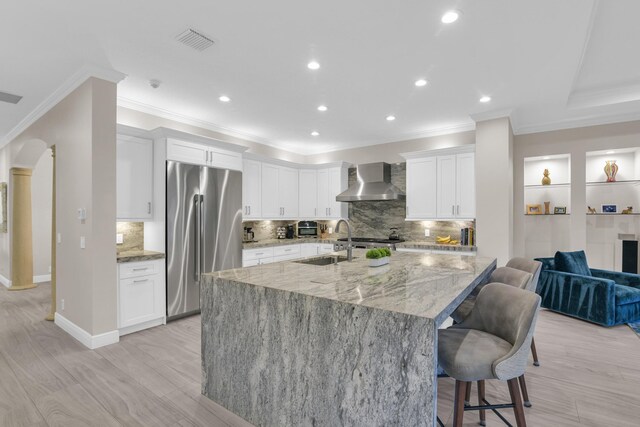 kitchen with backsplash, double oven range, wall chimney range hood, and white cabinetry