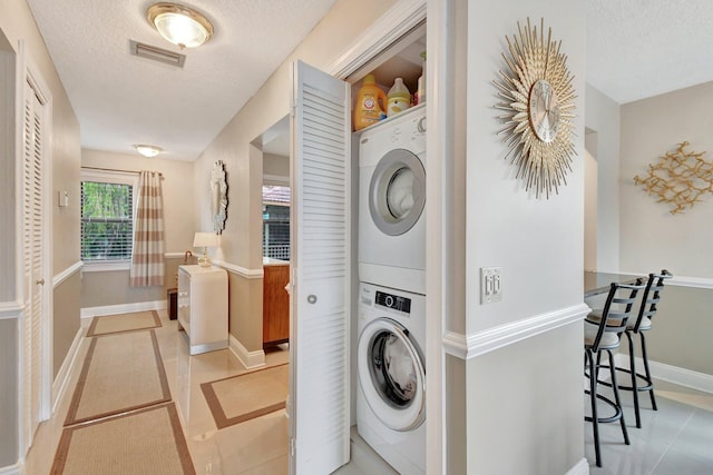 clothes washing area with stacked washing maching and dryer, a textured ceiling, and light tile patterned floors