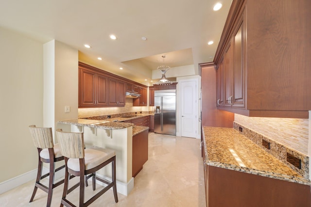 kitchen with decorative light fixtures, stainless steel built in fridge, light stone countertops, and kitchen peninsula