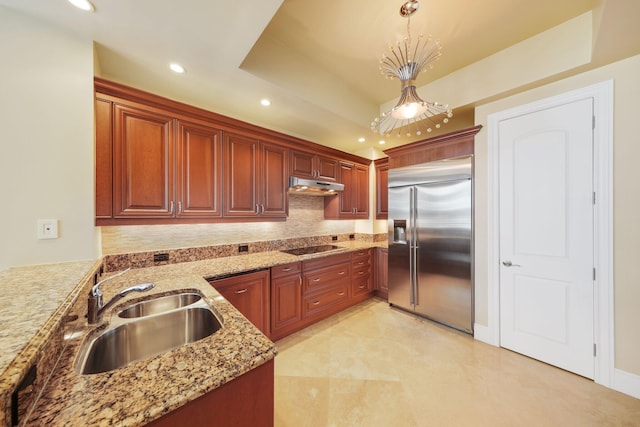 kitchen featuring light stone counters, stainless steel built in refrigerator, black electric cooktop, sink, and decorative light fixtures