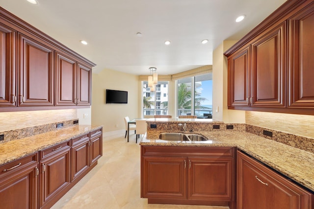 kitchen with backsplash, light carpet, sink, hanging light fixtures, and light stone counters