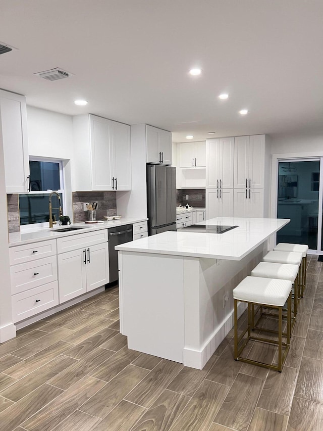 kitchen with visible vents, white cabinets, a kitchen island, light countertops, and black appliances