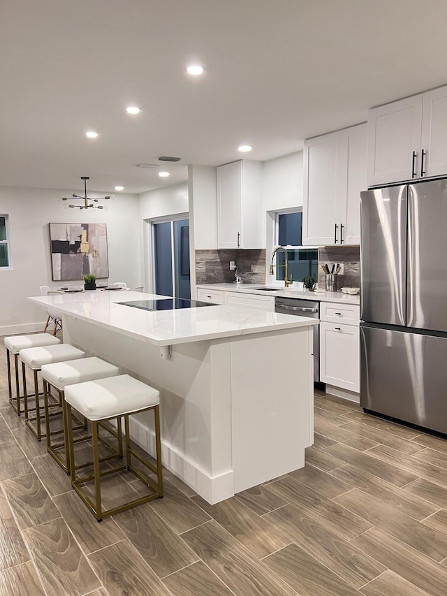 kitchen with stainless steel appliances, white cabinetry, a large island, and a kitchen bar