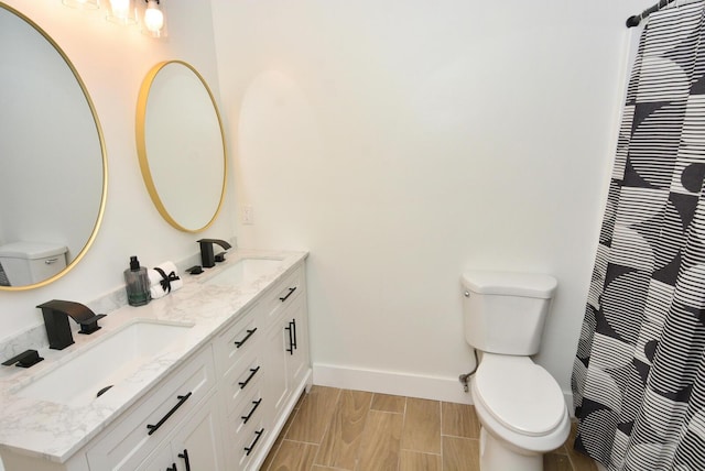 bathroom featuring double vanity, a sink, toilet, and baseboards