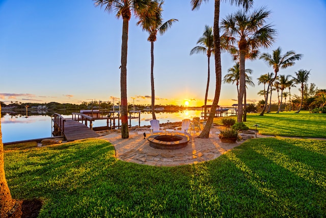 patio terrace at dusk with a fire pit, a dock, a water view, and a lawn