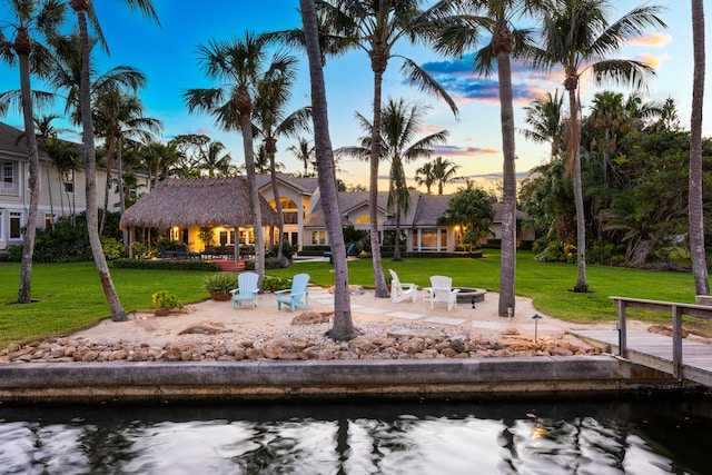 exterior space featuring a water view, a fire pit, a patio area, and a lawn