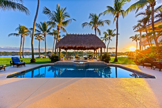 pool at dusk with a gazebo, a patio area, a yard, and a water view