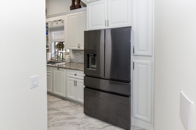 kitchen featuring backsplash, white cabinets, sink, stainless steel fridge, and stone countertops