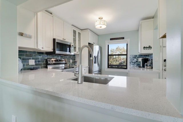 kitchen with backsplash, light stone counters, stainless steel appliances, sink, and white cabinetry