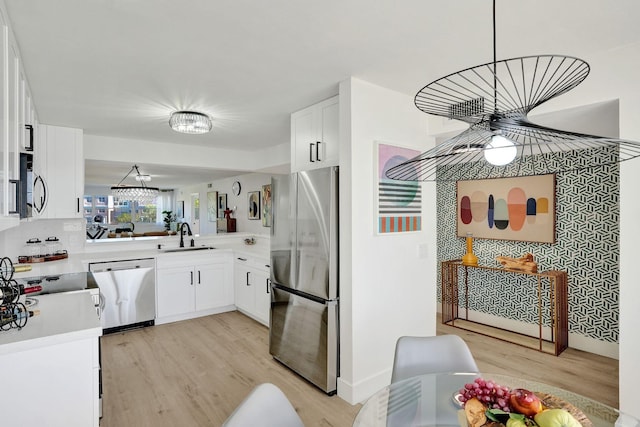 kitchen featuring sink, light hardwood / wood-style flooring, decorative light fixtures, white cabinets, and appliances with stainless steel finishes