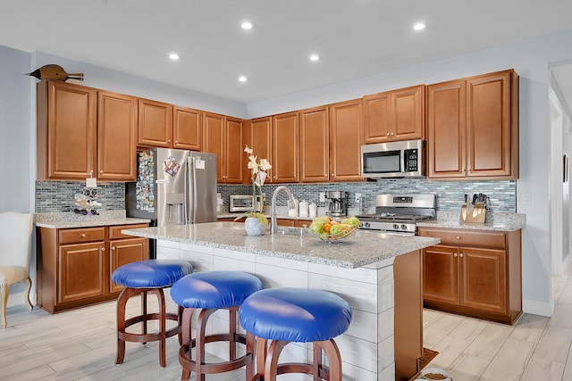 kitchen with a breakfast bar, stainless steel appliances, light stone counters, and a center island with sink