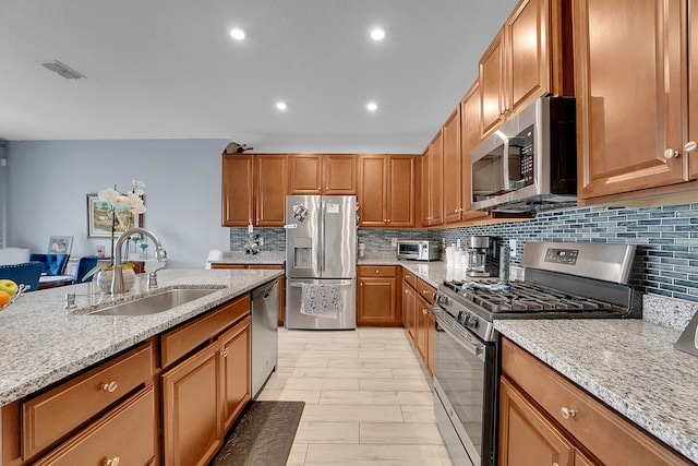 kitchen featuring decorative backsplash, light stone counters, sink, and appliances with stainless steel finishes