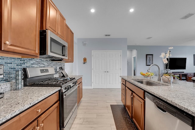 kitchen with sink, light stone countertops, tasteful backsplash, light hardwood / wood-style floors, and stainless steel appliances