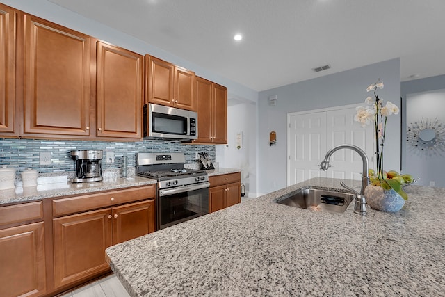 kitchen with decorative backsplash, appliances with stainless steel finishes, light stone counters, and sink