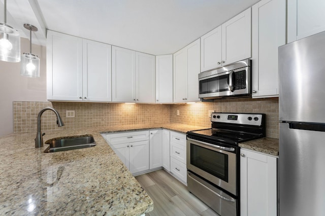 kitchen featuring light stone counters, decorative light fixtures, white cabinetry, appliances with stainless steel finishes, and sink