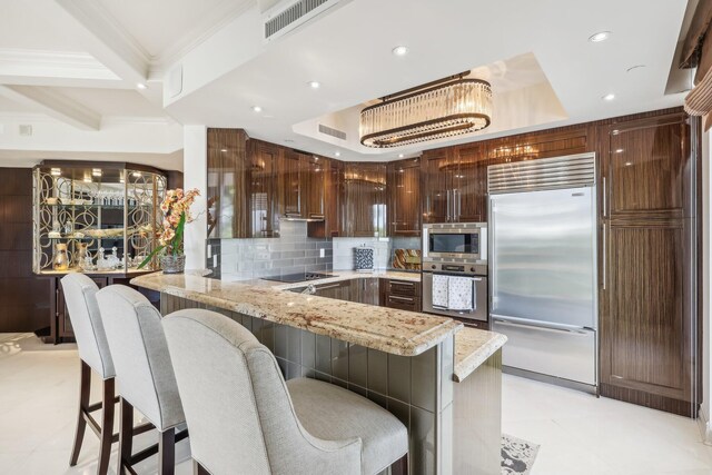 kitchen featuring built in appliances, light stone countertops, ornamental molding, a kitchen bar, and kitchen peninsula