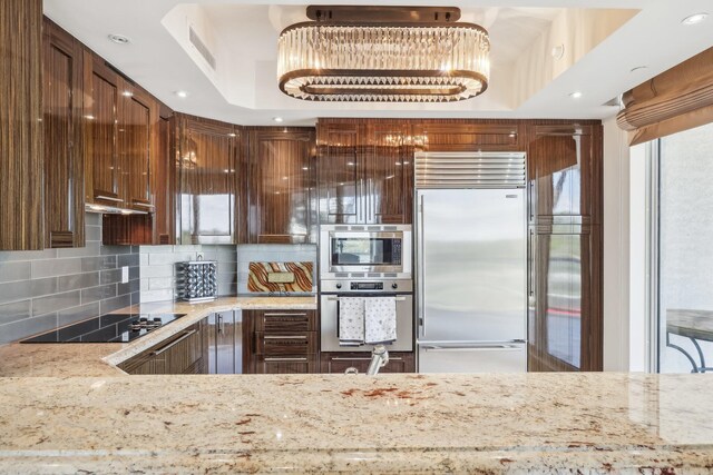 kitchen with light stone countertops, a kitchen breakfast bar, tasteful backsplash, built in appliances, and kitchen peninsula