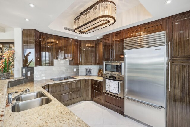 kitchen with decorative backsplash, built in appliances, a raised ceiling, and light stone countertops