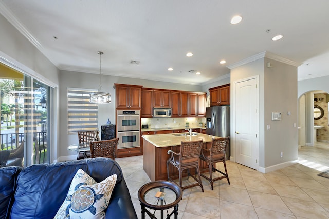 kitchen with a kitchen island with sink, sink, ornamental molding, decorative light fixtures, and stainless steel appliances