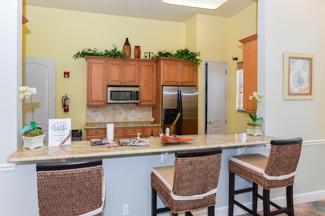 kitchen featuring kitchen peninsula, light stone countertops, tasteful backsplash, a breakfast bar, and stainless steel appliances