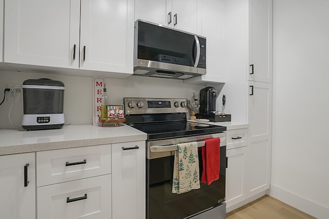 kitchen with light stone countertops, white cabinetry, stainless steel appliances, and light hardwood / wood-style flooring