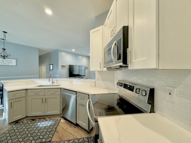 kitchen with sink, light hardwood / wood-style flooring, appliances with stainless steel finishes, decorative light fixtures, and kitchen peninsula