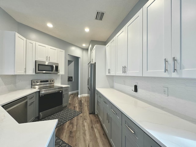 kitchen with gray cabinetry, dark wood-type flooring, tasteful backsplash, white cabinetry, and stainless steel appliances