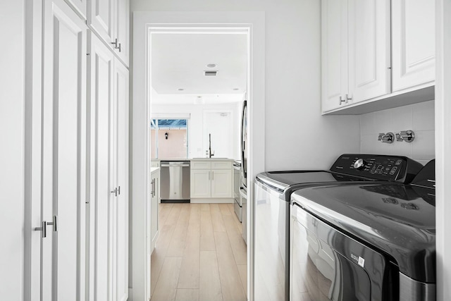 laundry room with cabinets, light hardwood / wood-style floors, and washing machine and dryer