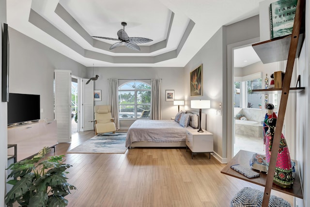 bedroom with a tray ceiling, ceiling fan, and light hardwood / wood-style flooring