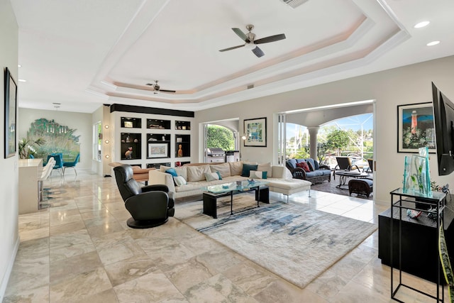 living room with built in shelves, a tray ceiling, and ceiling fan