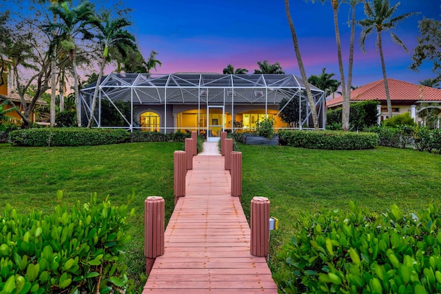 back house at dusk featuring a lanai and a yard