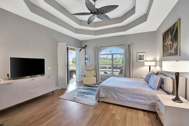 bedroom with light wood-type flooring, a tray ceiling, and ceiling fan