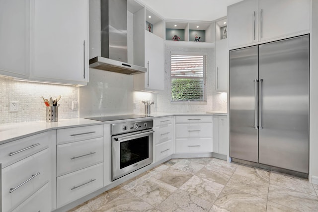 kitchen with tasteful backsplash, white cabinetry, wall chimney range hood, and appliances with stainless steel finishes