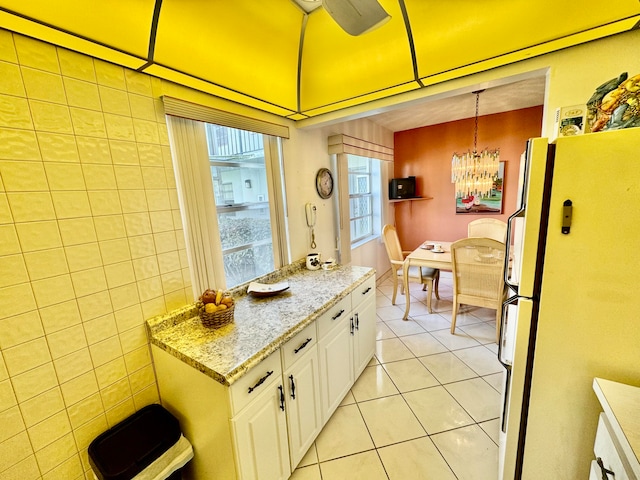 kitchen with white refrigerator, tile walls, white cabinets, hanging light fixtures, and light tile patterned flooring