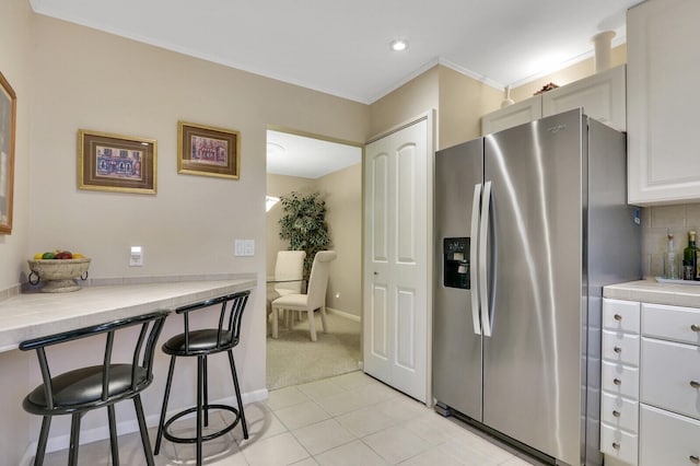 kitchen featuring stainless steel fridge, tasteful backsplash, a breakfast bar, white cabinets, and light tile patterned flooring