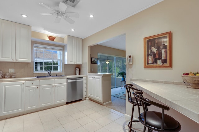 kitchen featuring sink, stainless steel dishwasher, tile countertops, decorative backsplash, and white cabinets