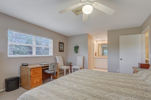 bedroom with ceiling fan, ensuite bathroom, light colored carpet, and a textured ceiling