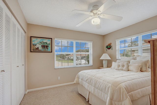 bedroom with a textured ceiling, ceiling fan, light carpet, and a closet