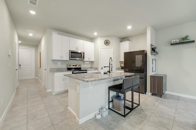 kitchen with light stone countertops, a kitchen breakfast bar, a kitchen island with sink, white cabinets, and appliances with stainless steel finishes