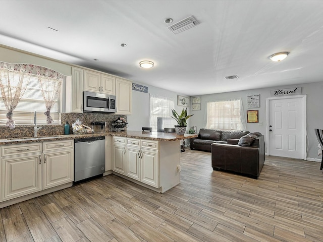 kitchen featuring sink, stainless steel appliances, kitchen peninsula, cream cabinetry, and light wood-type flooring