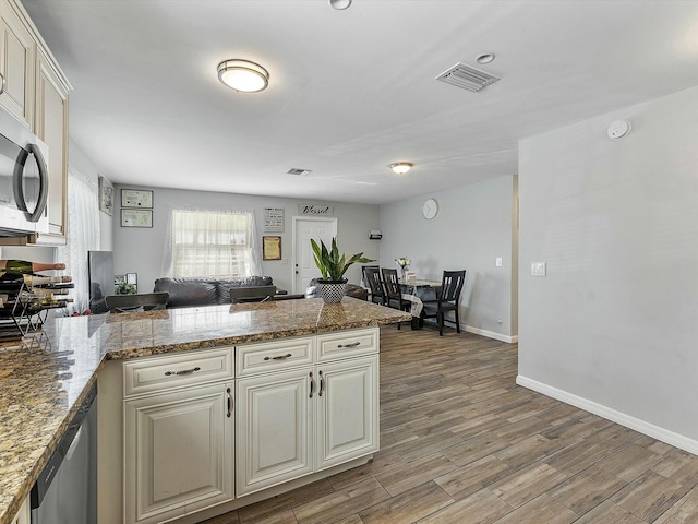 kitchen with kitchen peninsula, light stone counters, light hardwood / wood-style flooring, and stainless steel appliances